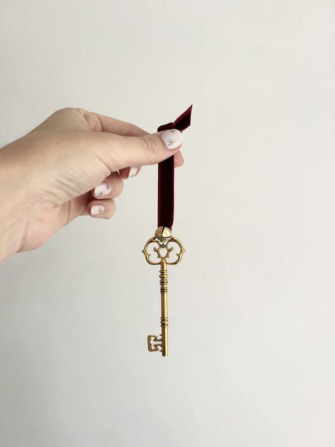 Golden Father Christmas Key attached to poem card and adorned with red velvet ribbon and small golden bell being held to show size