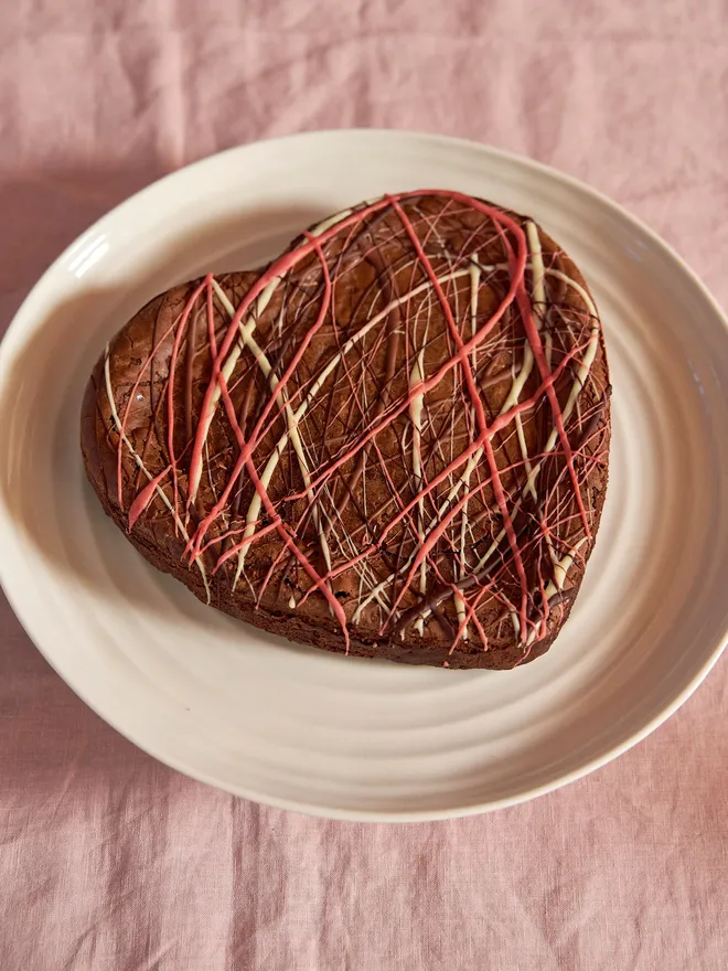 Valentines heart shaped decorated brownie on a textured white plate sitting on a pale pink tablecloth