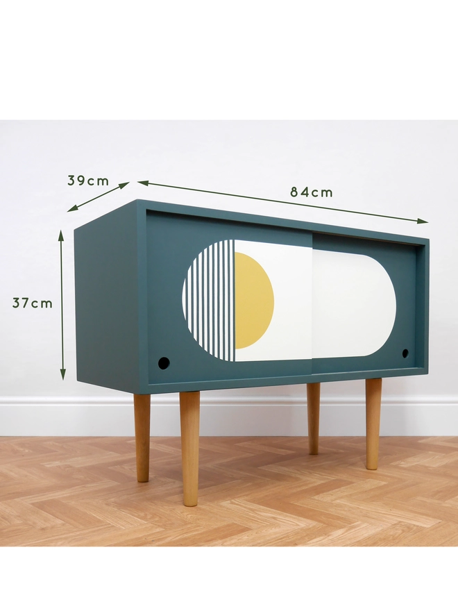 Teal mid-century record cupboard with sliding doors featuring bold geometric patterns in white and yellow.