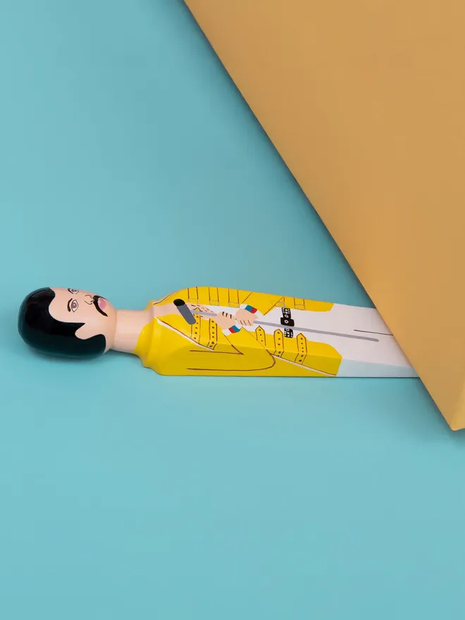 Wooden Door Stopper (Freddy), a colourful wooden door stop sitting under a door.