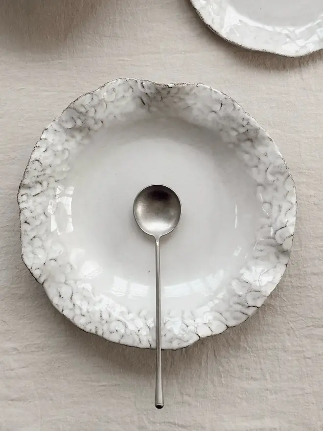 Dapple Stoneware Pasta Bowl, with a spoon placed on a table cloth. 