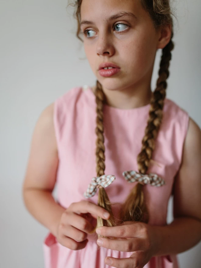 Girl with long brown hair in plaits with a pink dress and rust hair bows