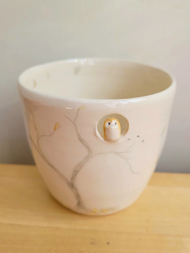 ceramic drinking cup for tea or ritual cacao with a miniature barn owl in a hole near the top of the cup there is a hand painted tree 