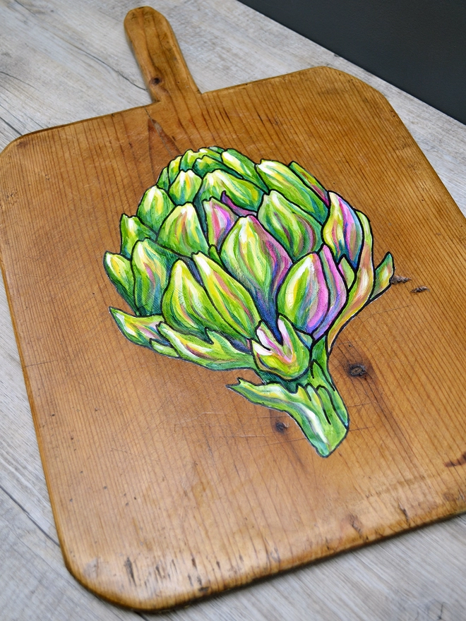 Close up of a wooden chopping board with handpainted design of an artichoke