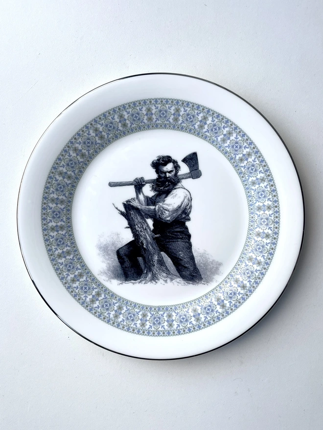 vintage plate hanging on a white wall, it has a decorative border, with a printed vintage illustration of a wild beard lumberjack in the middle 