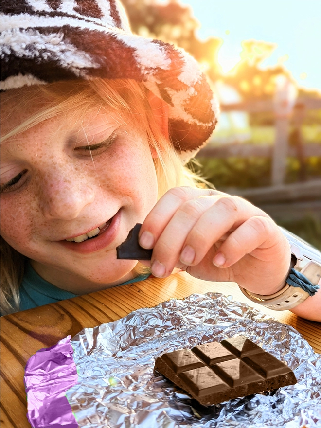 Happy smiling child enjoying silky smooth milk chocolate chunks in purple foil wrapper 
