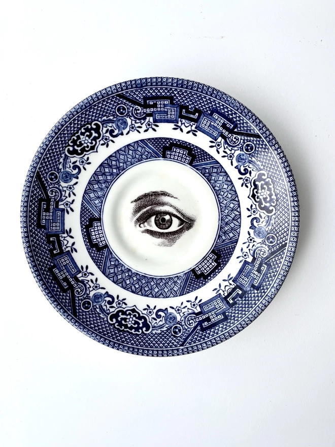 vintage plate with a blue and white ornate border, with a printed vintage illustration of an eye in the middle 
