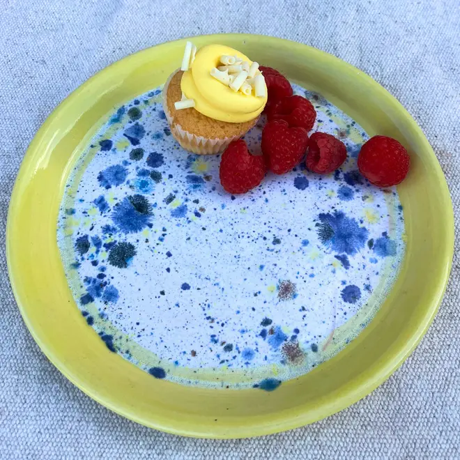Shoreline Side Plate, a colourful plate placed on a stone surface. It is accompanied by fruits and a sweet treat. 