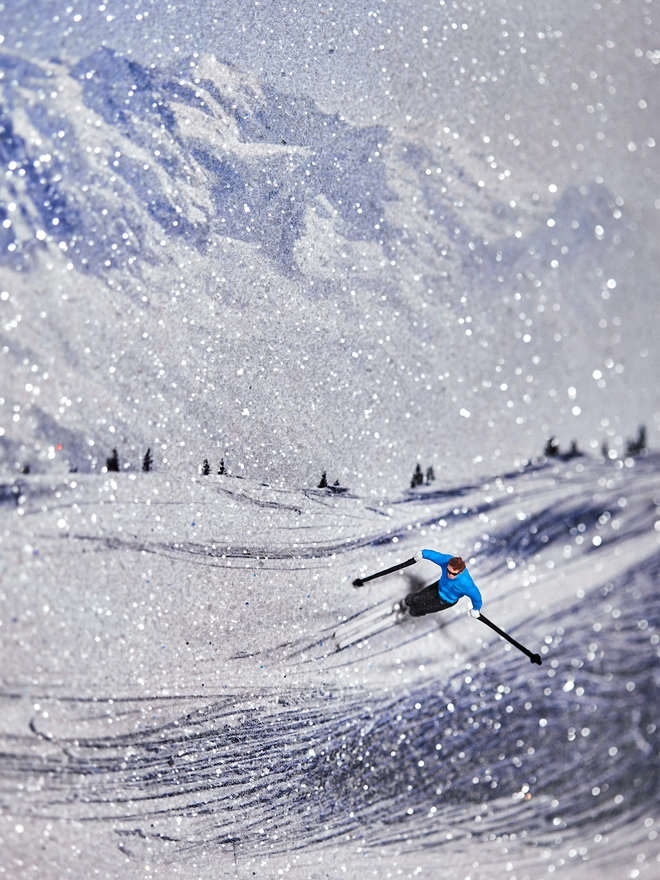 Miniature scene in an artbox showing a tiny male skiing figurine skiing against a sparkling mountainous backdrop 