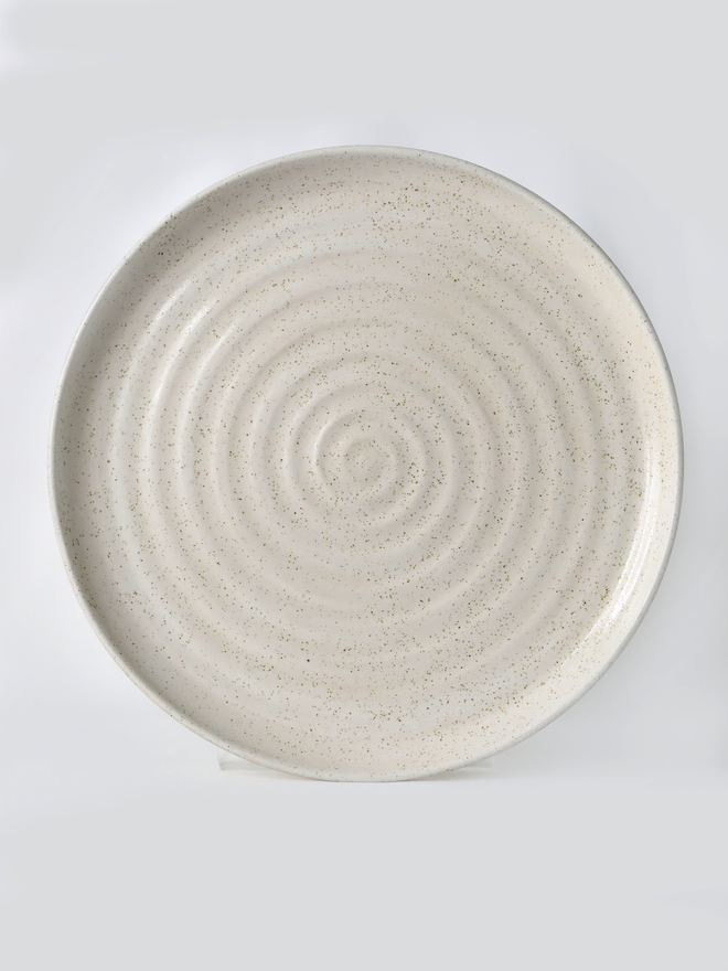 A handmade ceramic lunch plate in glossy pepper white glaze, photographed from above against a plain light grey background, showing a natural concentric swirl texture from the wheel-throwing process