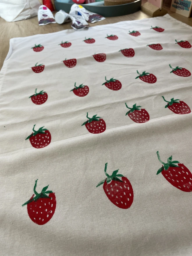Cotton kitchen tea towel with strawberry pattern laid on a wooden table.