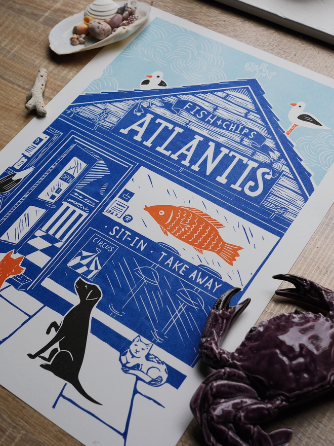 A blue, orange and black print of a fish and chip shop called Atlantis, outside there are waiting 2 dogs, a cat and some seagulls