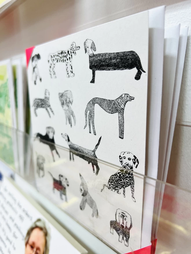 A card featuring hand drawn black dogs arranged in a pattern on a white background on a rack 
