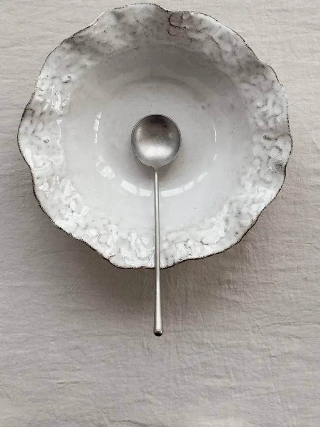 Dapple Stoneware Cereal & Salad Bowl, with a spoon, placed on a table cloth. 