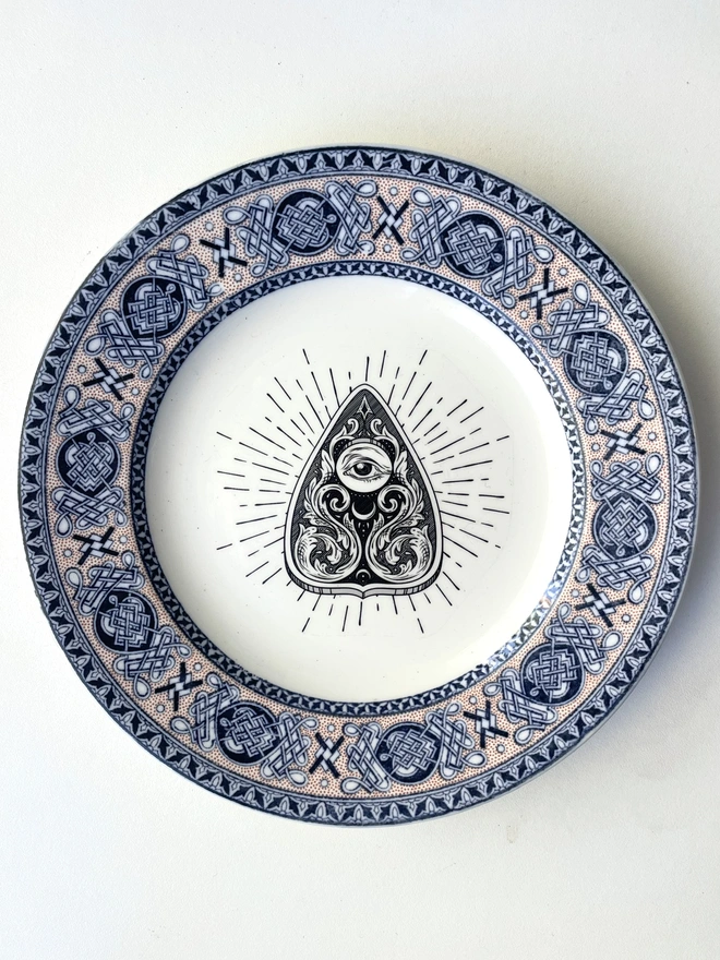 vintage plate with an ornate border, with a printed vintage illustration of a Ouija planchette in the middle 
