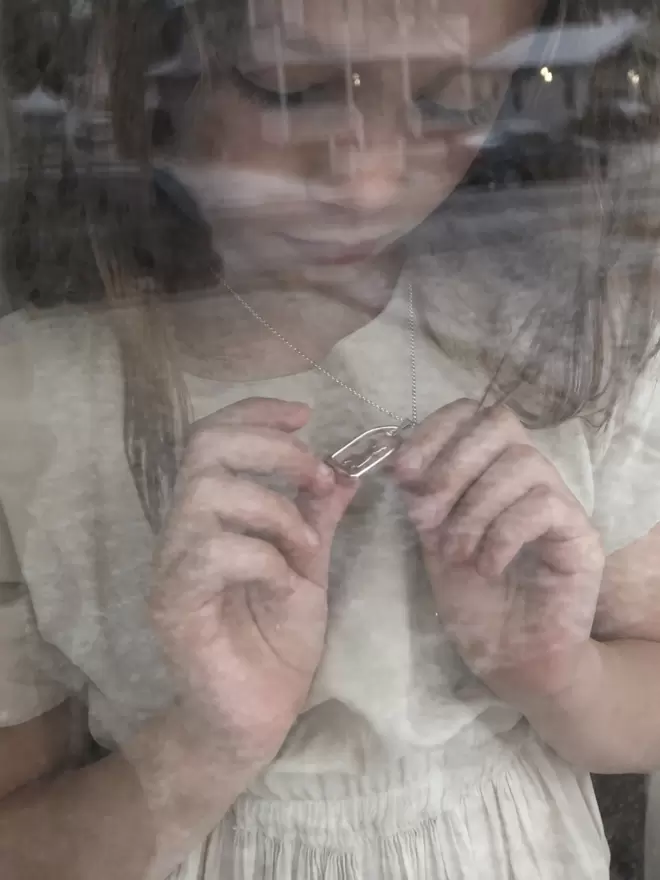 View through glass of child carefully holding silver pendant and looking down towards