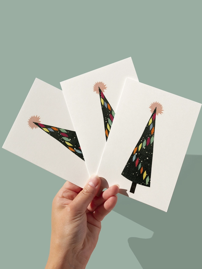 A mid century style greeting card featuring a black christmas tree decorated with colourful baubles and a pink star.