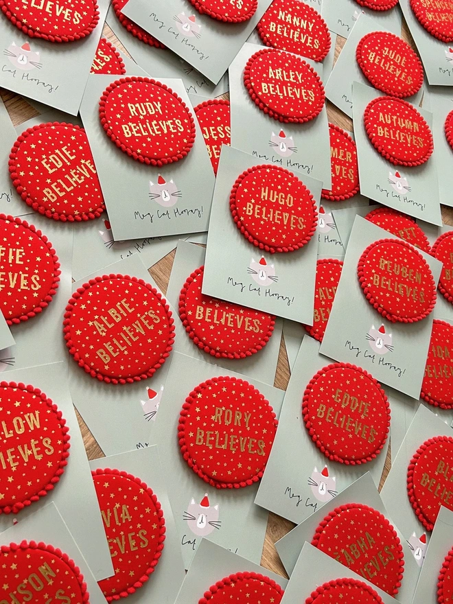 Red christmas 'Believe' badges with gold stars and a red pom pom trim and a child's name 