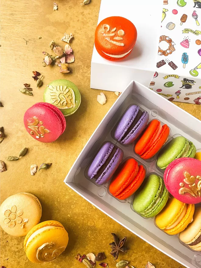 colourful Diwali themed macarons with gold henna designs in a white box on a gold background with rose petals