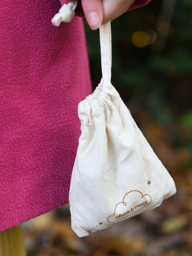 A natural cotton bag is being held beside someone in a pink coat.