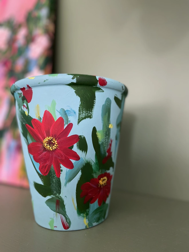Hand painted pale teal plant pot with vibrant red zinnia flowers