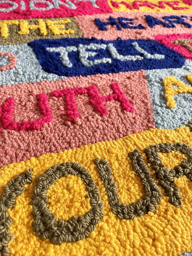 Close up of typographic textile art 'I didn't have the heart to tell the truth about your art' in primary colours on patchwork background