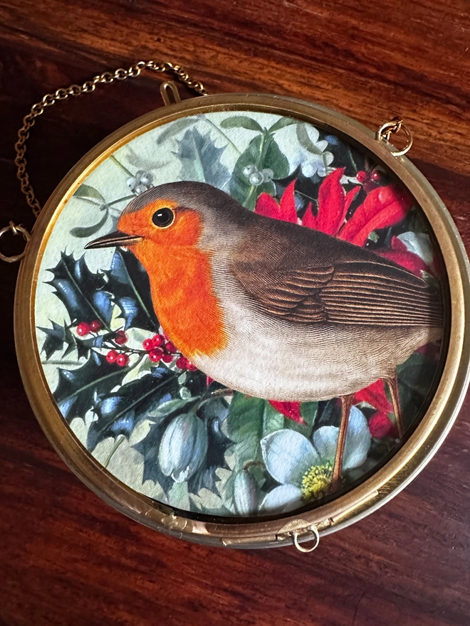 A robin amongst Christmas foliage miniature print in a gold, brass hanging frame.