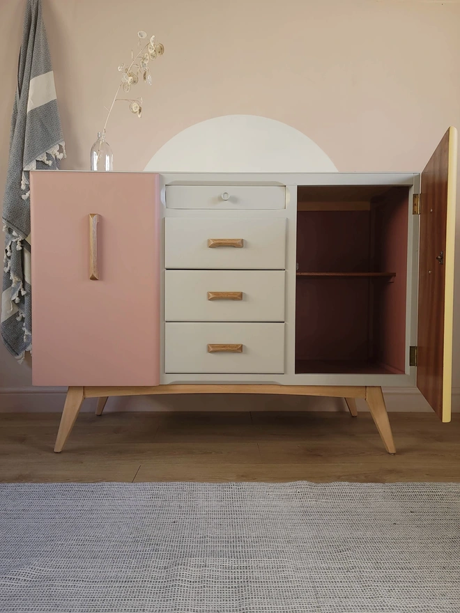 Mid-century vintage sideboard painted with a pink cupboard door, cream drawers and open door painted dark pink inside with a pink wall behind