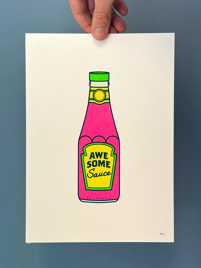 hand holding an A4 screen print of an iconic bottle of tomato ketchup in flouro colours. The label reads 'Awesome Sauce'