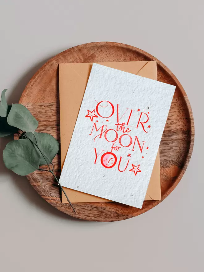 Plantable Card with ‘Over the Moon for you’ with star illustrations on a wooden tray next to a Eucalyptus branch