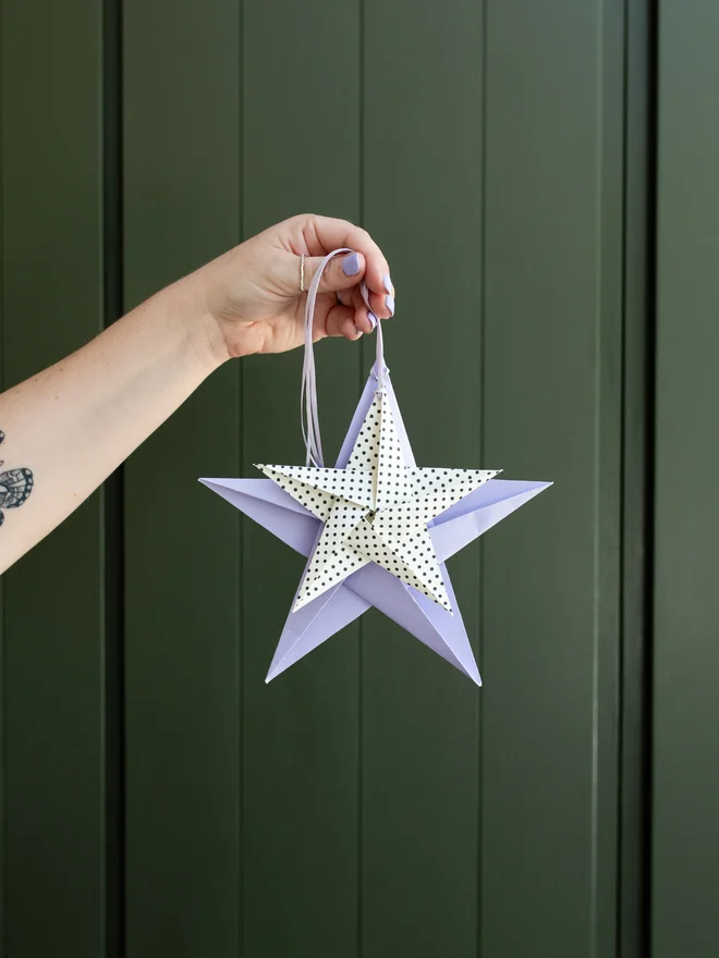 Women holding out 2 origami stars hanging on ribbon