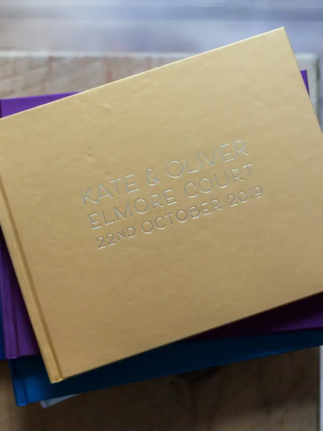 Personalised Wedding Guest Book With Crisp Font, stack of guest books on a wooden surface. 