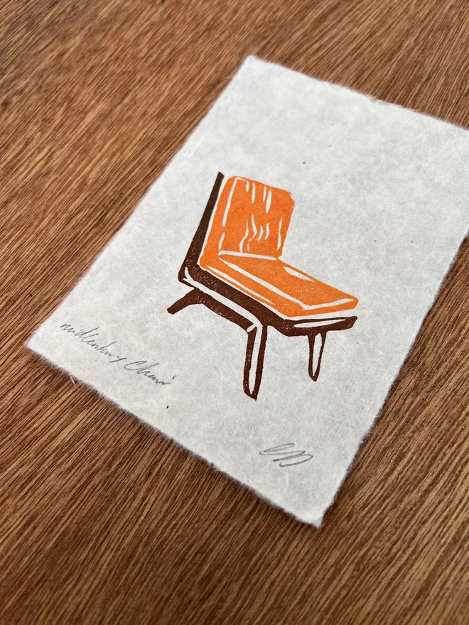 Hand-printed mini vintage orange chair lino print on natural handmade paper, featuring a bold retro illustration of a mid-century chair.