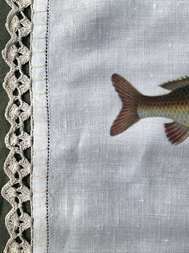 Detail of the crochet and stitch work edge of a linen cloth that has a fish print