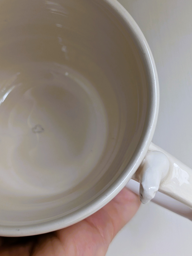 aerial shot of a white cup with a close up of a ceramic polar bear sitting on the handle with a white heart inside the cup the cup