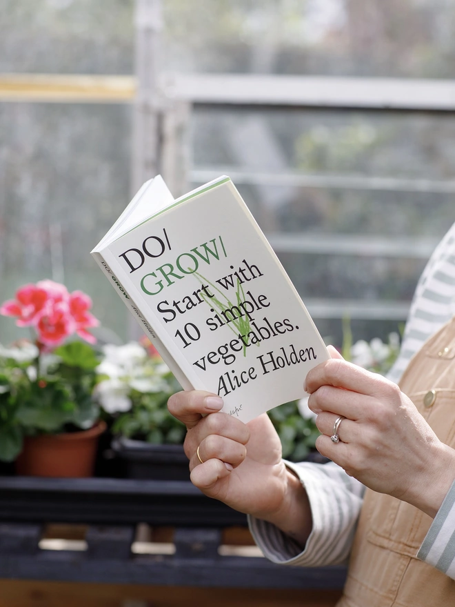 Woman holding paperback book in greenhouse