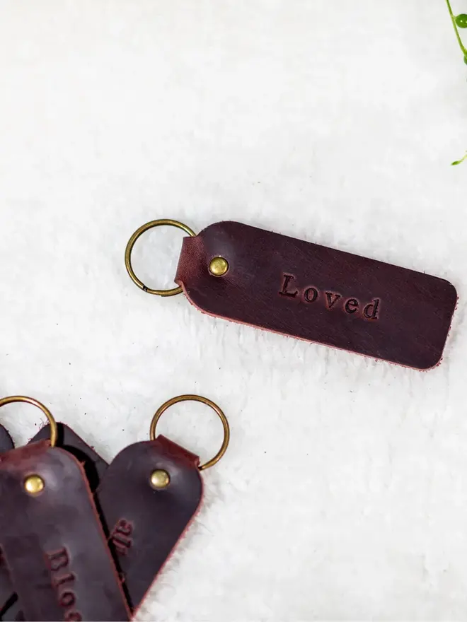custom leather embossed keyring. a dark brown leather keyring embossed with 'love' photographed against a white background.