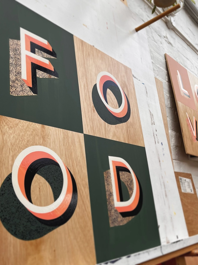 FOOD hand painted sign in coral, green and aubergine, in the artist's studio, at an angle. 