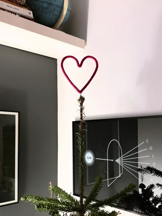 Close up of simple heart topped Xmas tree in the corner of a grey and white room 