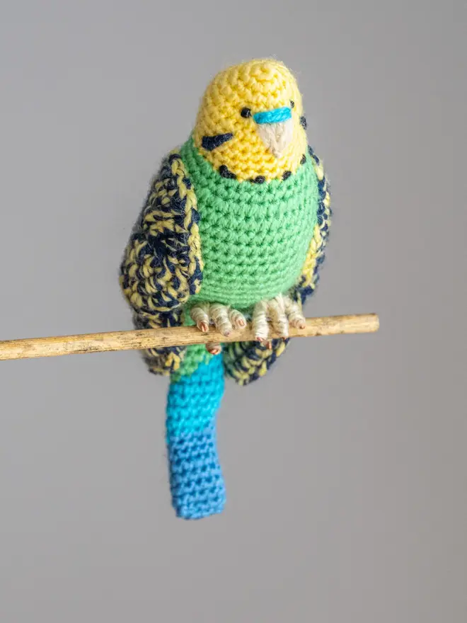 Budgerigar Hand Crocheted Figure, a green  crocheted bird sitting on a wooden poll. 