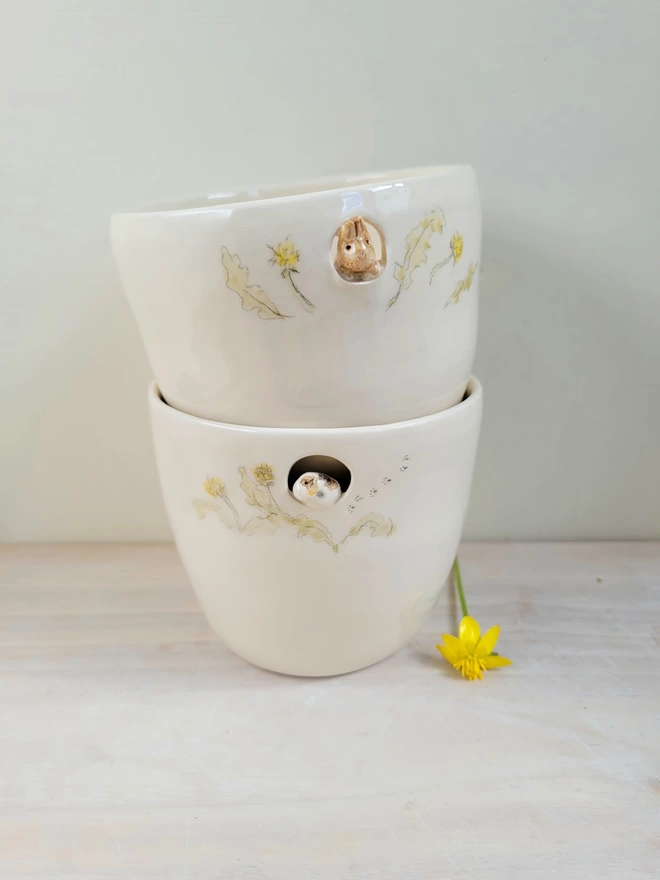 handmade ceramic handleless cup with a tiny guinea pig or bunny rabbit and dandelions