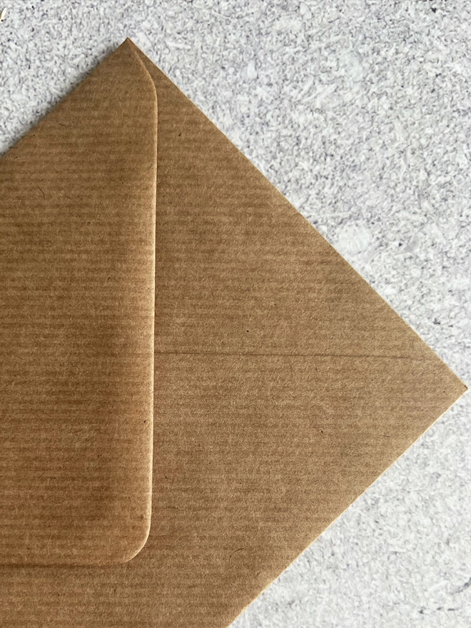 Close up of the lined texture of the brown envelope that comes with this card against a stone background.