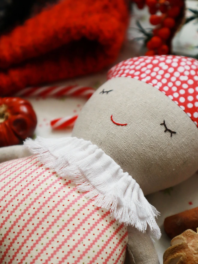Soft handmade mushroom-themed doll with a red spotted cap, embroidered smiling face, ruffled white collar, red-striped body, and small green feet.