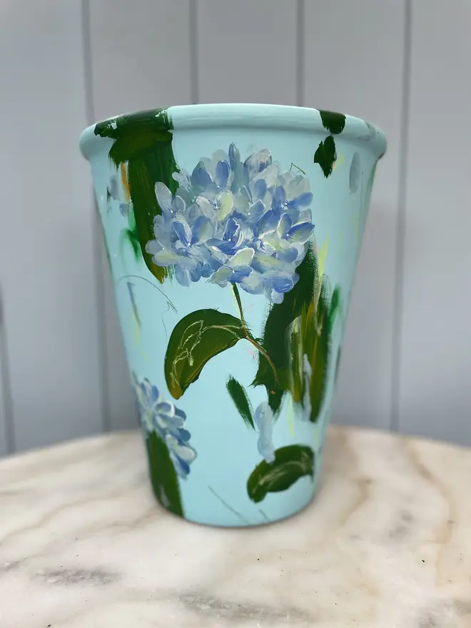 Hand painted terracotta floral plant pots pale blue background adorned in blue hydrangea flowers  
