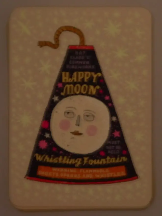 A Flash Of Brilliance Moon Firework Screenprint, a colourful firework design in the centre of a white screenprint. The glow in the dark design can be seen as well. 