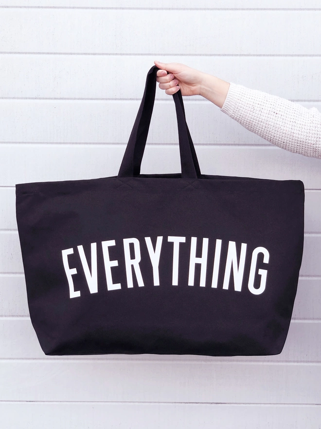 model holding out an oversized black canvas tote bag with everything slogan