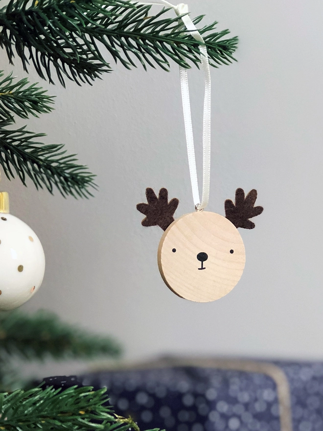 A small wooden and felt reindeer decoration hangs on a Christmas tree branch.