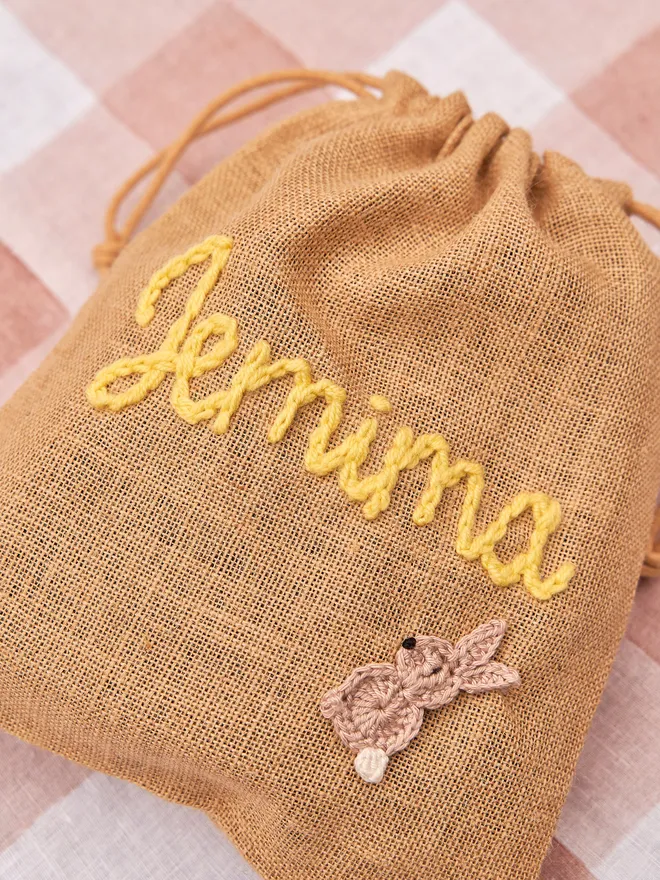 jute drawstring sack with brown knitted bunny decoration and yellow 'jemima' name  on red gingham table cloth