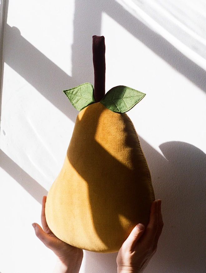 Golden pear cushion with green leaves held up 