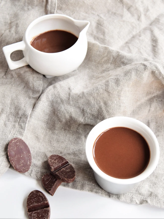 Jug of vegan-friendly hot chocolate and small cup of handmade hot chocolate with chocolate pieces